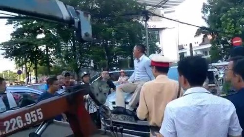 Tài xế đeo kính đen ngồi lên nắp capô phản đối CSGT cẩu xe