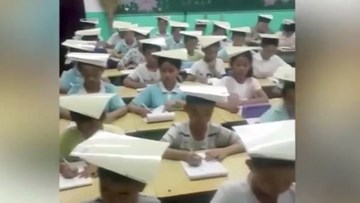 Học sinh tiểu học vừa đội sách vừa viết bài để rèn tư thế ngồi học
