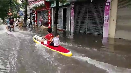 Hai em bé ngồi thuyền lướt sóng trên đường phố đông gây tranh cãi